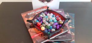 Bronboeken voor Dungeons and Dragons gestapeld onder een dice tray, die op zijn beurt weer gevuld is met allerlei verschillende soorten dobbelstenen.
