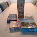 Vijf korte bordspellen bij elkaar op een tafel. In beeld zijn Onitama, De Crew, On Sale, Valse Motten en Rollecate.