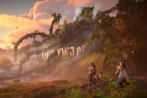 Een screenshot van Horizon: Forbidden West DLC Burning Shores. Aloy en Seyka lopen langs het vernietigde Hollywoodbord van Los Angeles.