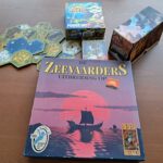 Vijf essentiële uitbreidingen naast elkaar. Het modulaire bord van Scythe, de Power Up! uitbreiding van King of Tokyo, een doos van Magic en Zeevaarders van Catan.