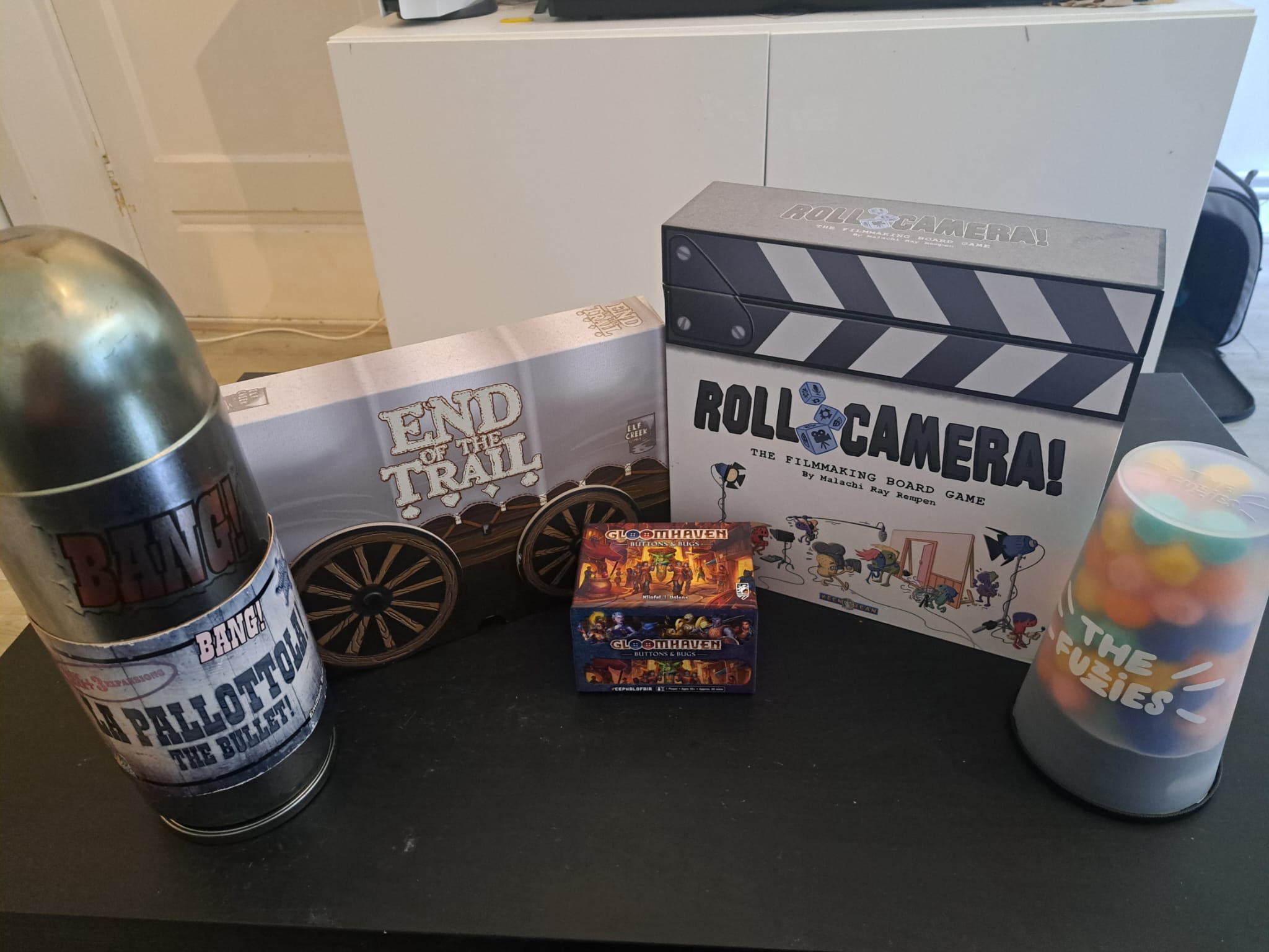 Vijf bijzondere spellendozen in mijn kast. Je hebt de Bullet-editie van Bang, End of the Trail, Roll Camera, The Fuzzes en Gloomhaven: Buttons & Bugs opgesteld in een semicirkel met Gloomhaven vooraan.